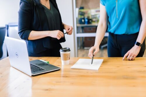 two women look at paper and laptop