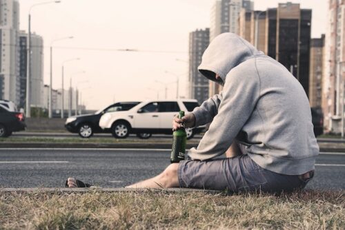 man sitting on road with alcohol container