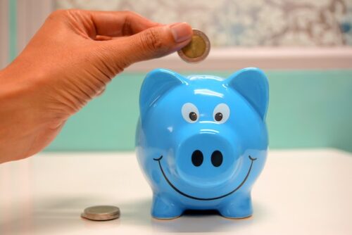 person putting coins in blue piggy bank